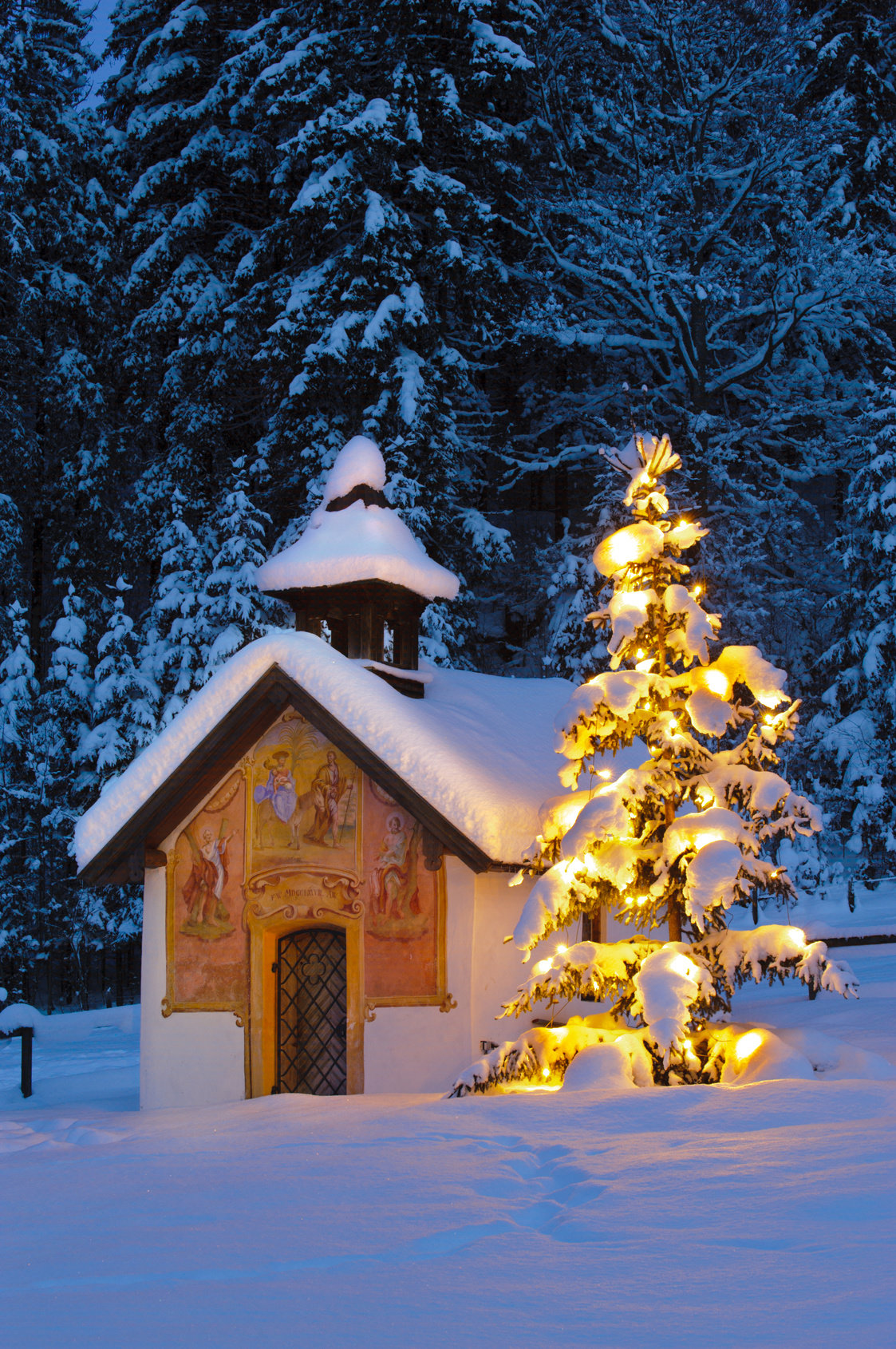 Eine Kapelle und ein geschmückter Weihnachtsbaum in einer Schneelandschaft